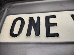 One way metal sign 16 inch long and 1 inch deep with hangers on back.